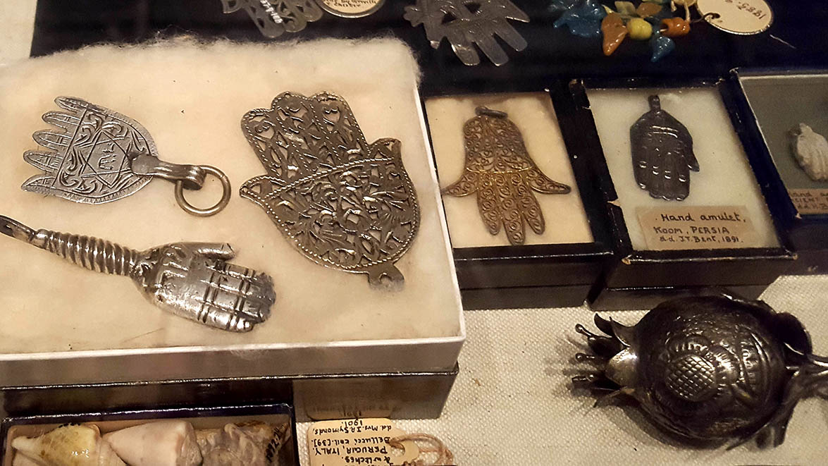 Metal hand amulets with handwritten labels displayed in glass cabinets in The Pitt Rivers Museum